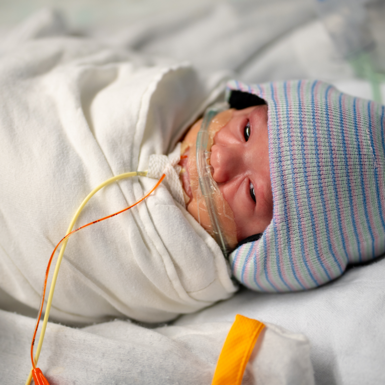 A newborn wearing a striped beanie in a hospital nursery