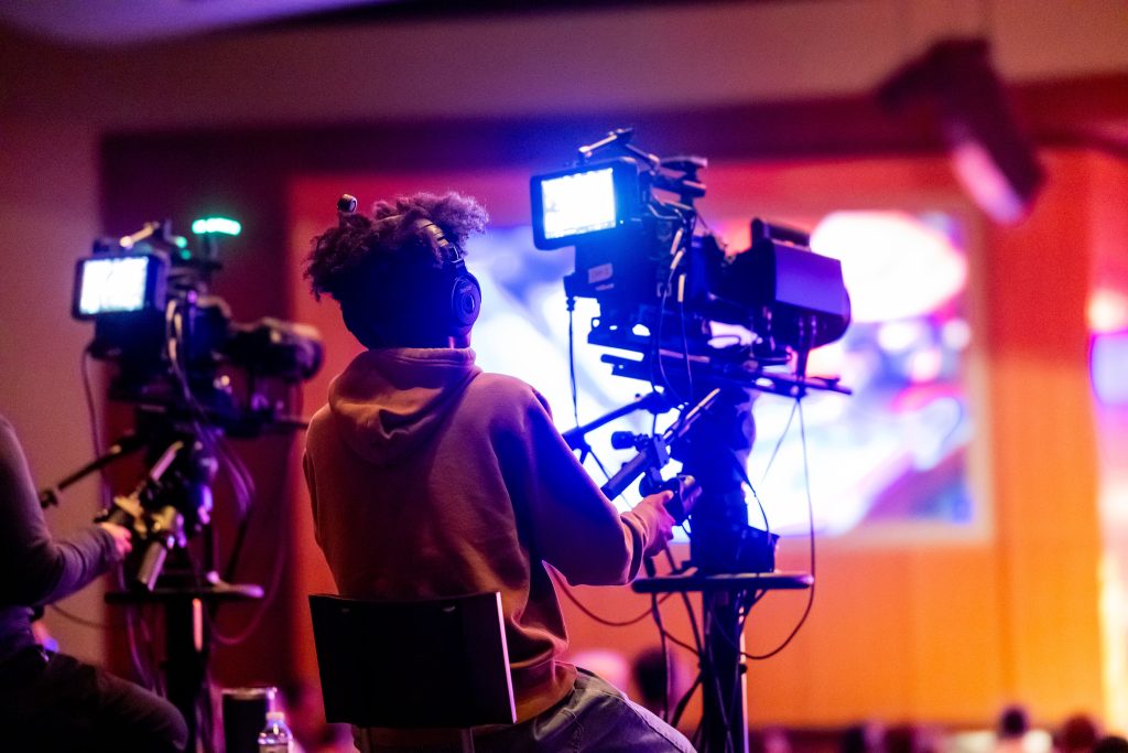 A camera operator films under colorful studio lights during a production