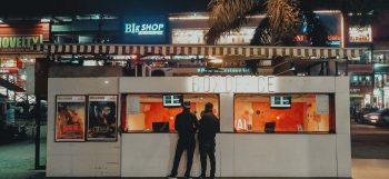 Two people standing at a box office under neon lights at night, urban cinema setting