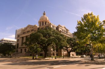 Historic domed courthouse building behind large oak trees on a sunny day