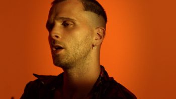 A portrait of the singer JMSN against an orange background.
