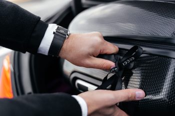 Close-up of hands unpacking an elegant suitcase from a car trunk, showcasing luxury fashion