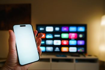A smartphone in focus with a smart TV displaying apps in a cozy living room