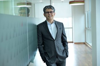 Smiling businessman standing confidently in a modern office hallway, wearing a suit